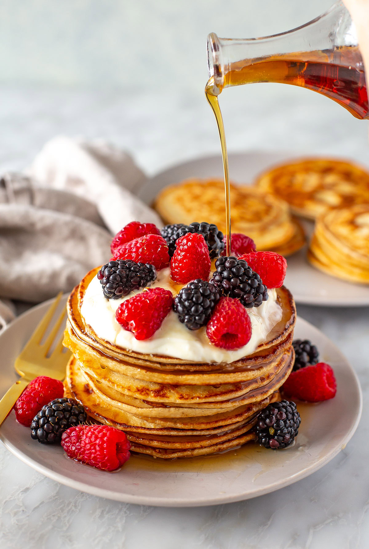 Side shot of maple syrup being poured over a stack of pancakes with berries.