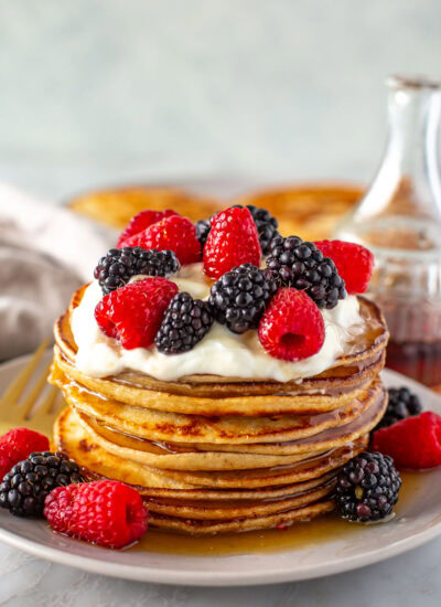 Side shot of a tall stack of Greek yogurt pancakes with berries and cream.