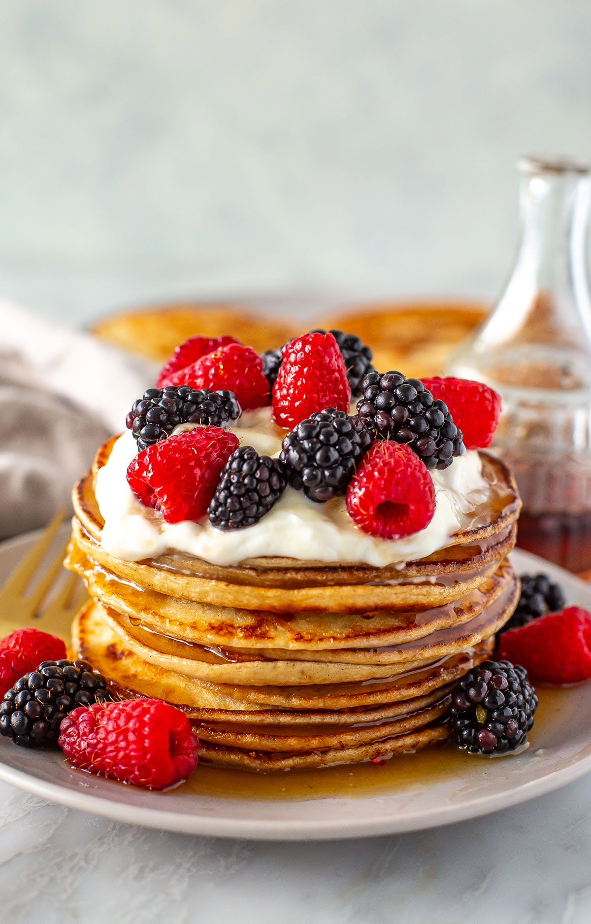 Side shot of a tall stack of Greek yogurt pancakes with berries and cream.