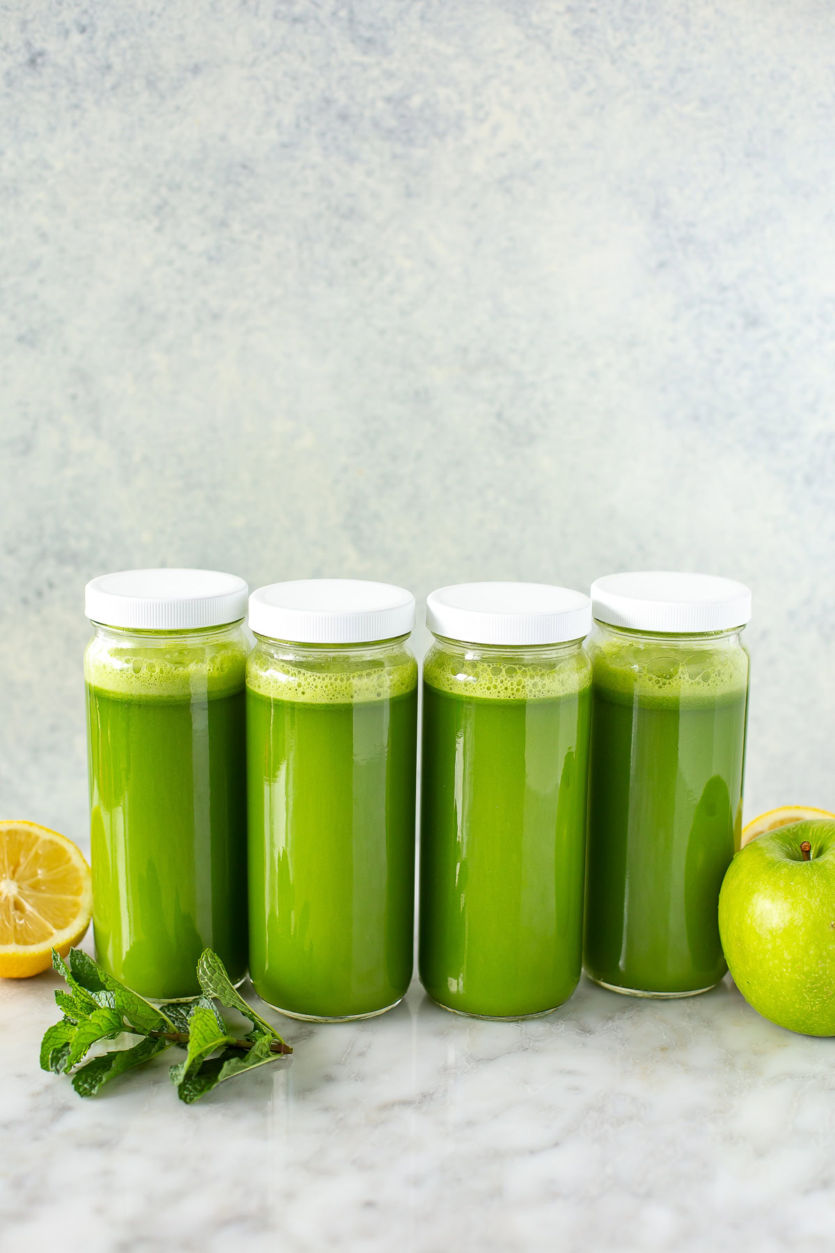Side shot of four sealed jars of green juice with fruit and mint.