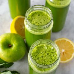 Overhead shot of green juice in four glasses with lemons and mint.