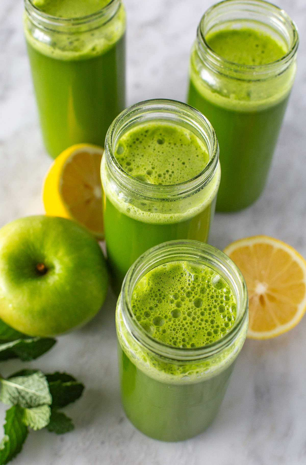 Overhead shot of green juice in four glasses with lemons and mint.
