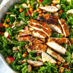 Overhead shot of a bowl of kale crunch salad with sliced chicken and dressing on the side.
