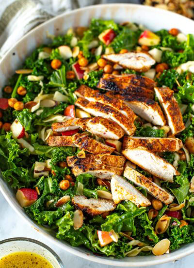 Overhead shot of a bowl of kale crunch salad with sliced chicken and dressing on the side.