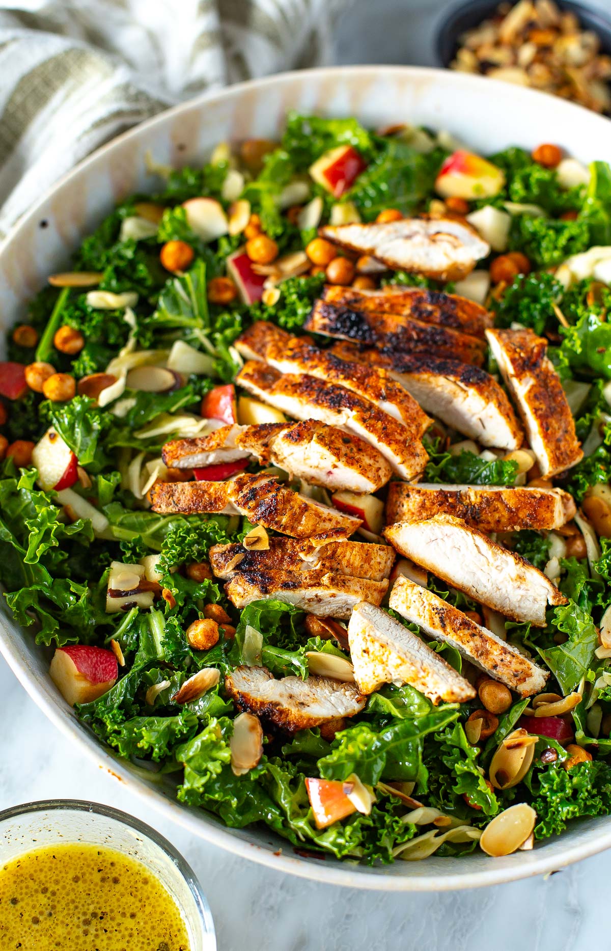 Overhead shot of a bowl of kale crunch salad with sliced chicken and dressing on the side.