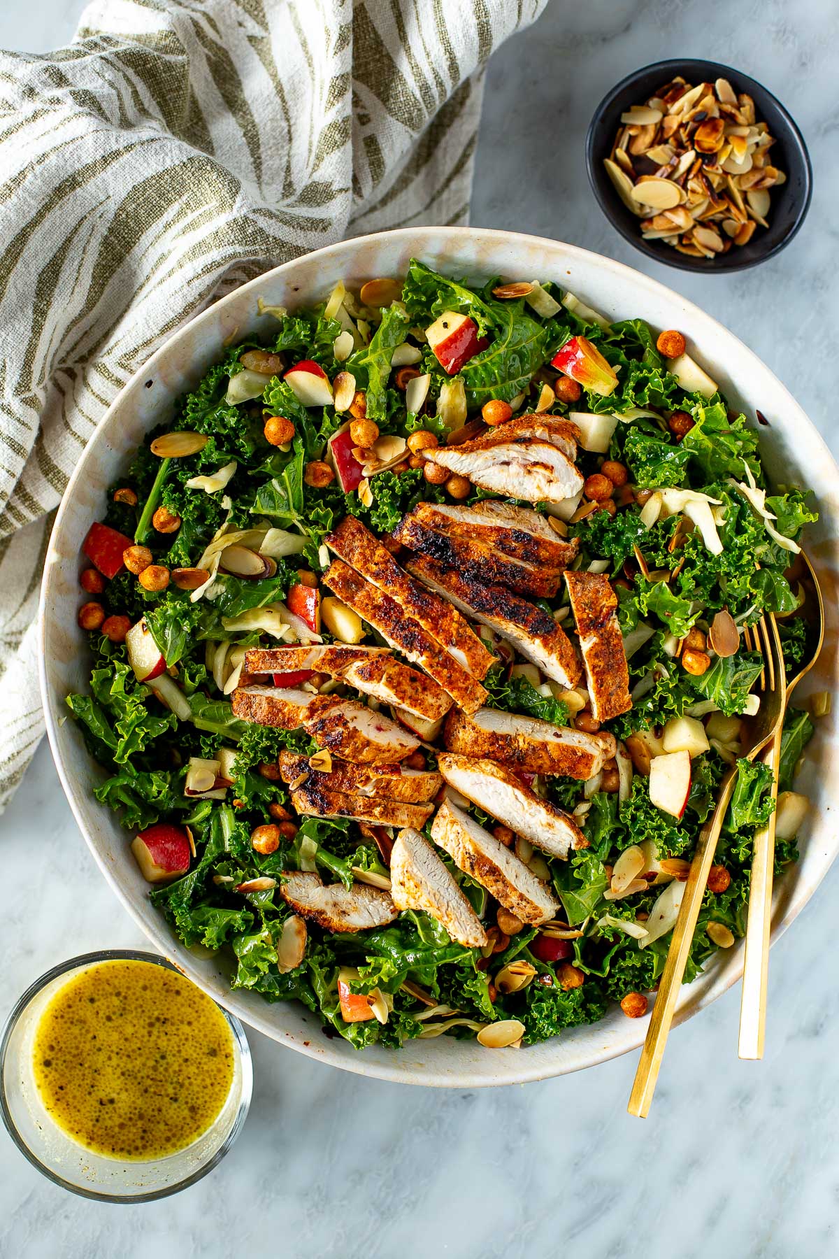 Overhead shot of a bowl of kale crunch salad with chicken, a fork, and a side of dressing.