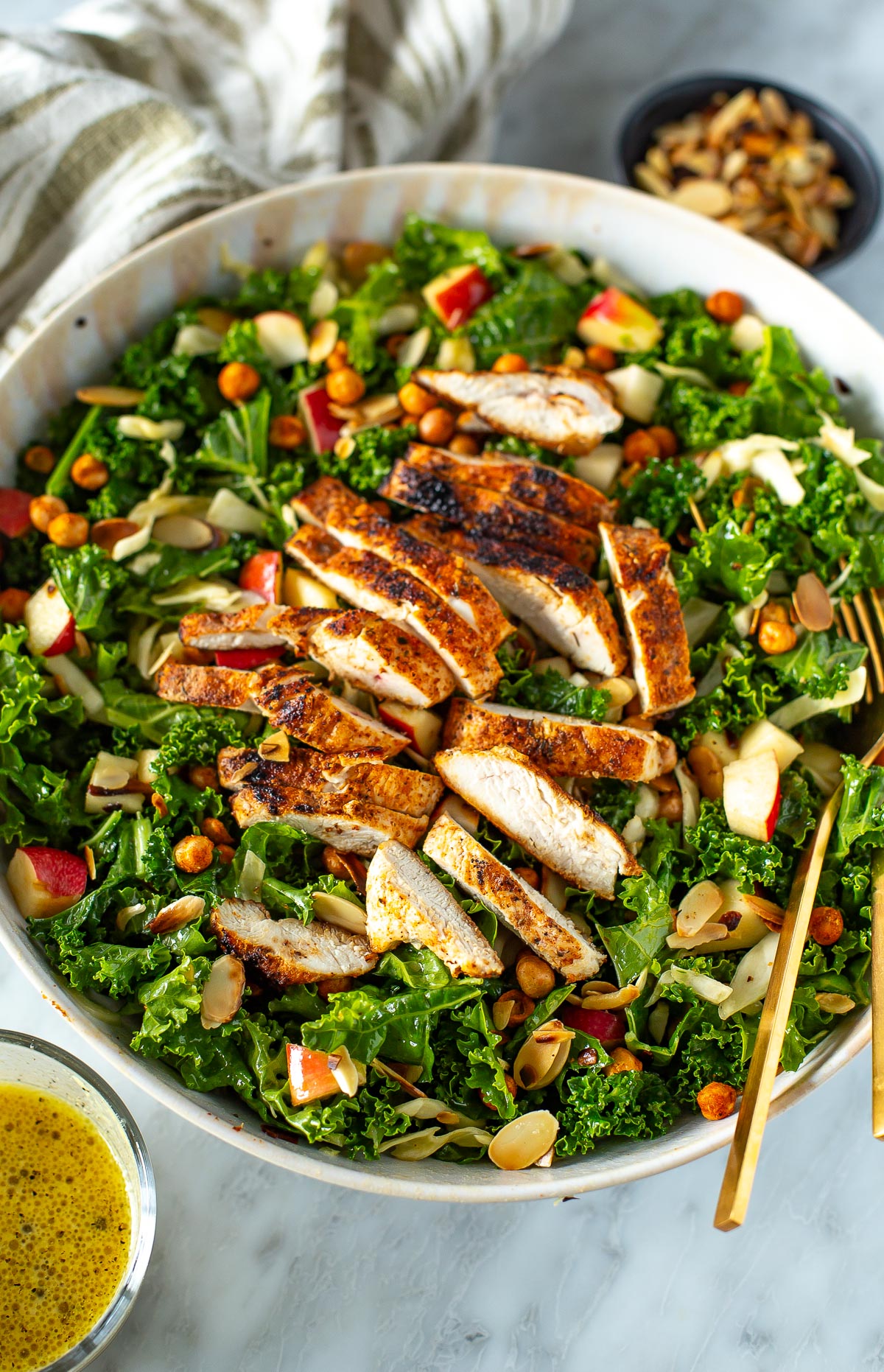 Overhead shot of a bowl of kale crunch salad with chicken, a fork, and a side of dressing.