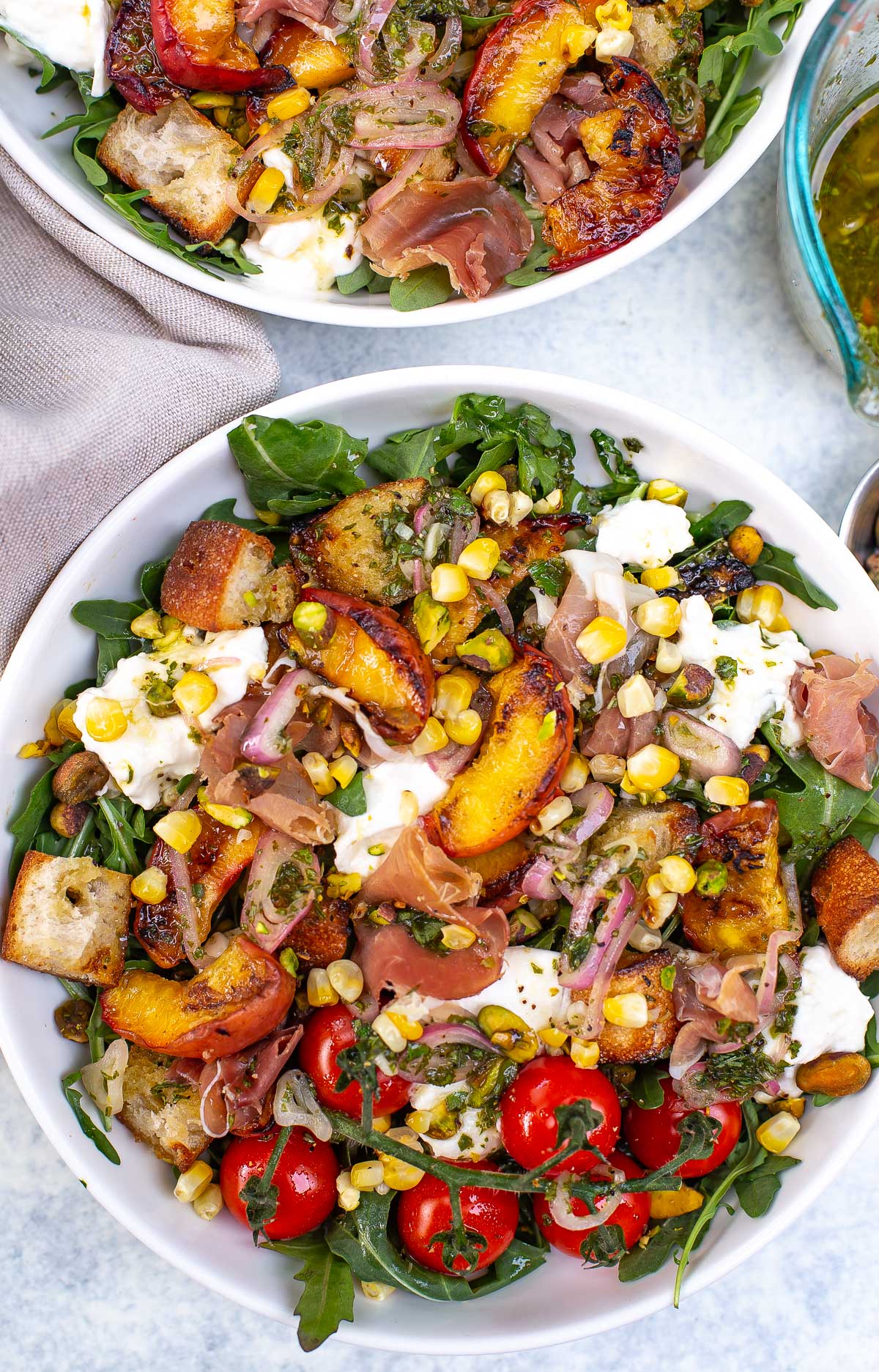 Overhead shot of two bowls of grilled peach burrata salad with various toppings.