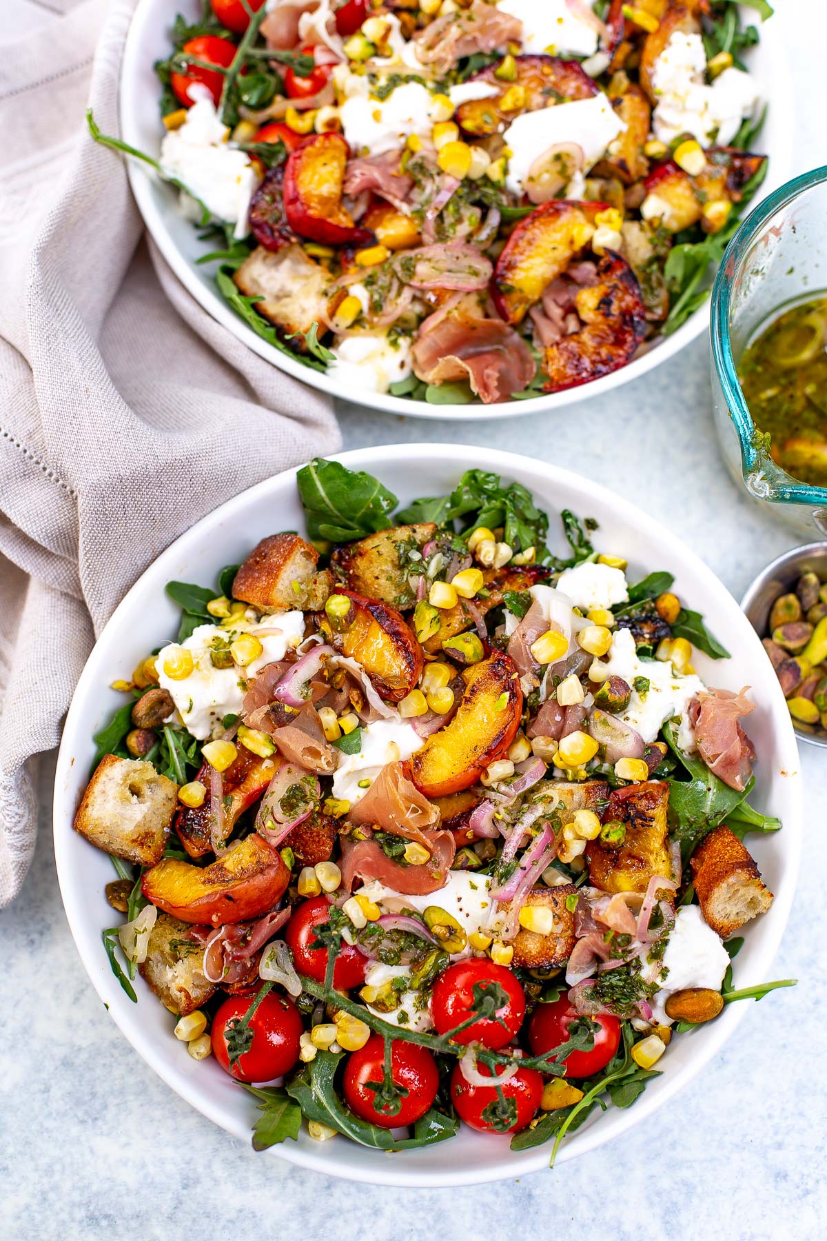 Overhead shot of two bowls of grilled peach burrata salad with various toppings.