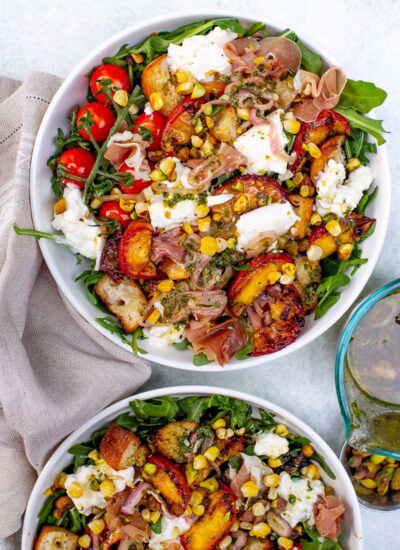 Overhead shot of two bowls of grilled peach burrata salad with various toppings.