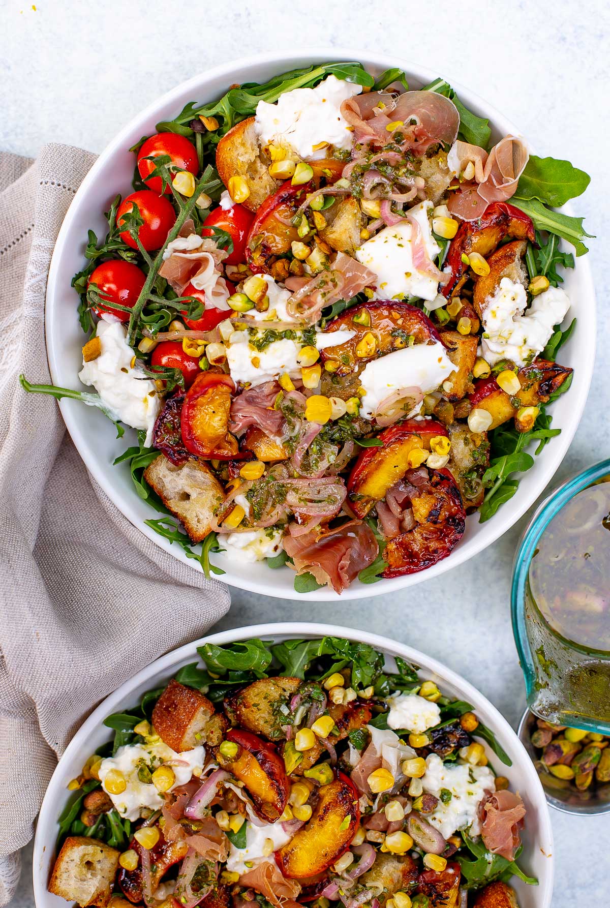 Overhead shot of two bowls of grilled peach burrata salad with various toppings.