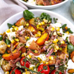 Close-up shot of a bowl of grilled peach burrata salad with various toppings.