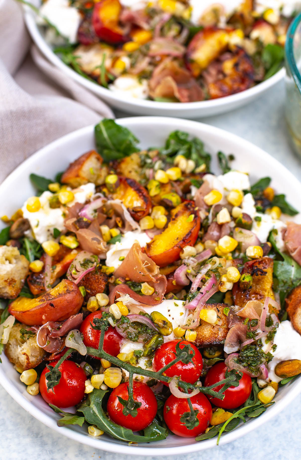 Close-up shot of a bowl of grilled peach burrata salad with various toppings.