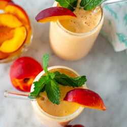 Overhead shot of two peach smoothies garnished with peach slices and mint leaves.
