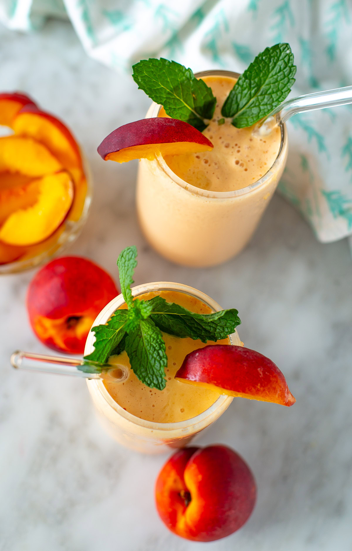 Overhead shot of two peach smoothies garnished with peach slices and mint leaves.