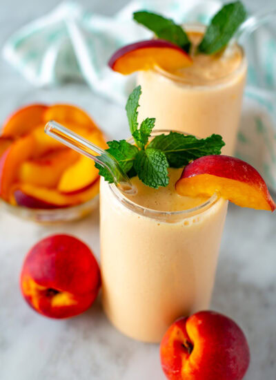 Side shot of two peach smoothies garnished with peach slices and mint leaves.