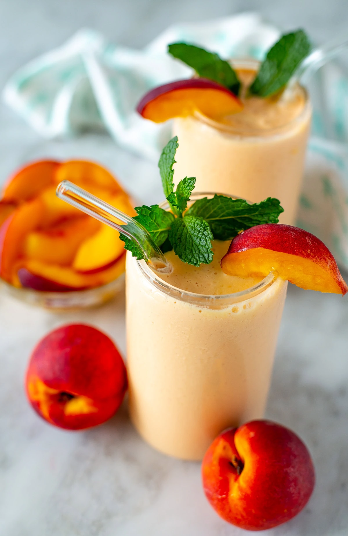 Side shot of two peach smoothies garnished with peach slices and mint leaves.