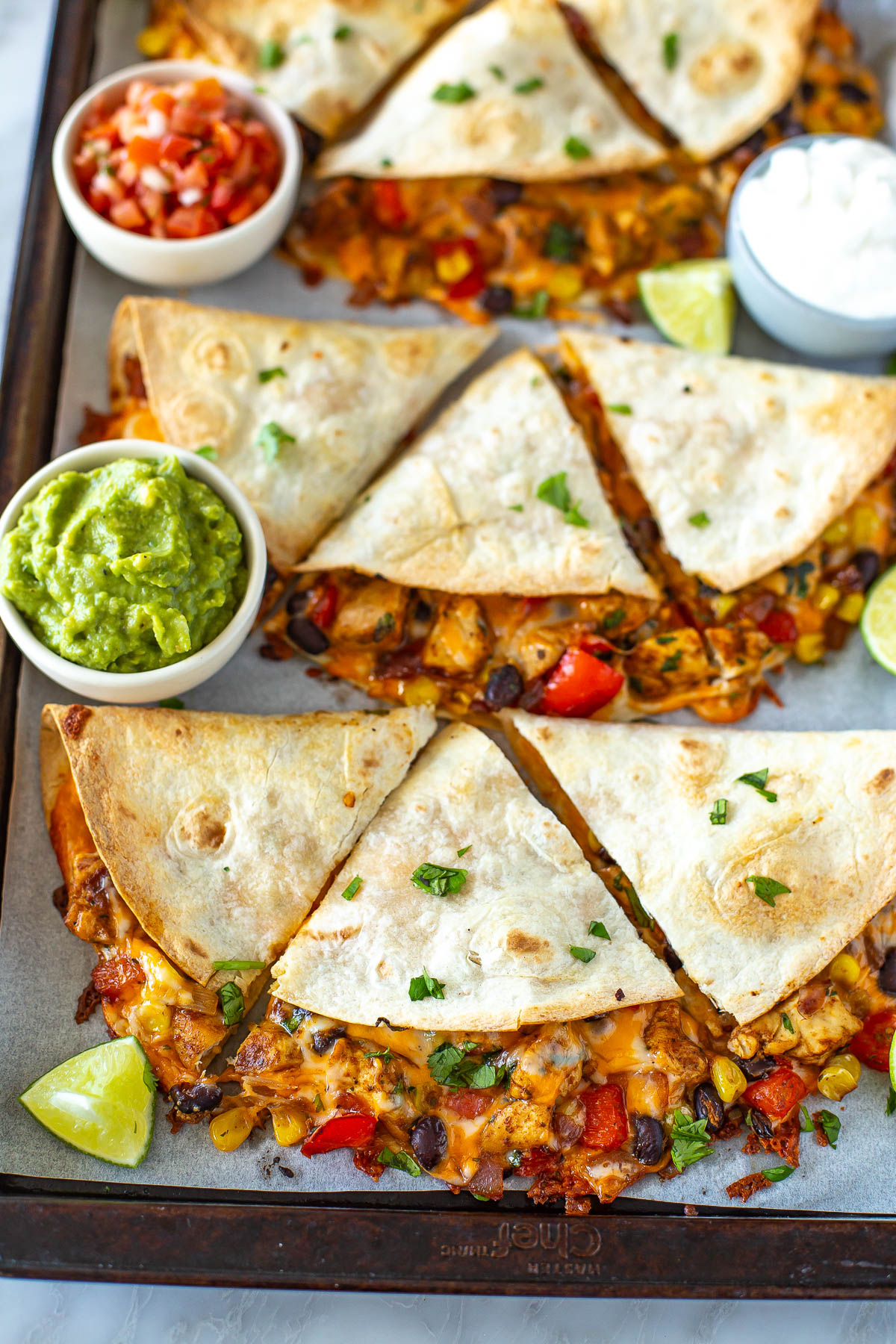 Overhead shot of a sheet pan full of finished quesadillas with side bowls of guacamole and salsa.