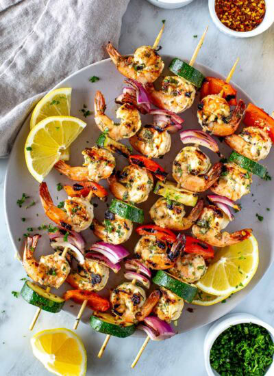 Overhead shot of cooked shrimp and vegetable skewers garnished with lemon and herbs on a serving platter 1