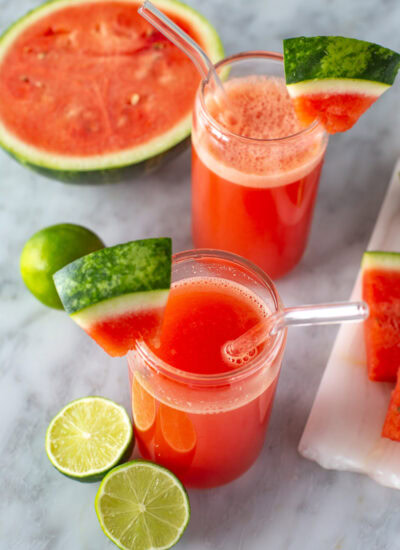 Overhead shot of two glasses of watermelon juice with garnishes and fruit.