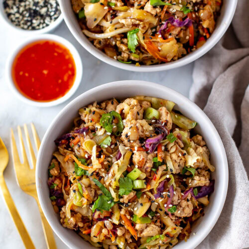 Overhead shot of two bowls of egg roll in a bowl with sauces and garnishes.