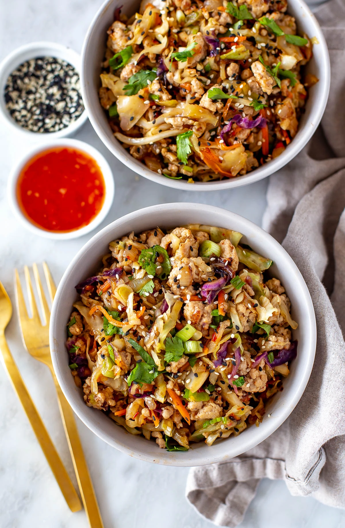 Overhead shot of two bowls of egg roll in a bowl with sauces and garnishes.