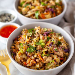 Side shot of two bowls of egg roll in a bowl with sauces and garnishes on the side.