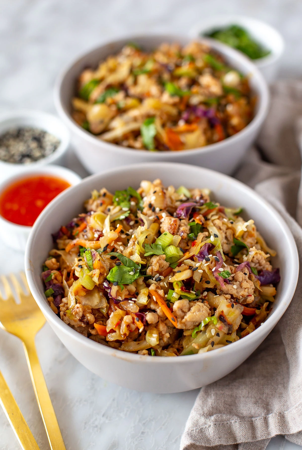 Side shot of two bowls of egg roll in a bowl with sauces and garnishes on the side.