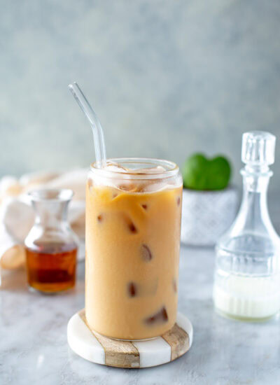 Side shot of an iced vanilla latte in a clear glass with ice and a straw on a coaster.