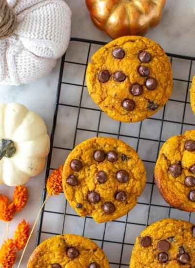Overhead shot of pumpkin protein muffins with chocolate chips on a cooling rack with decorative pumpkins.