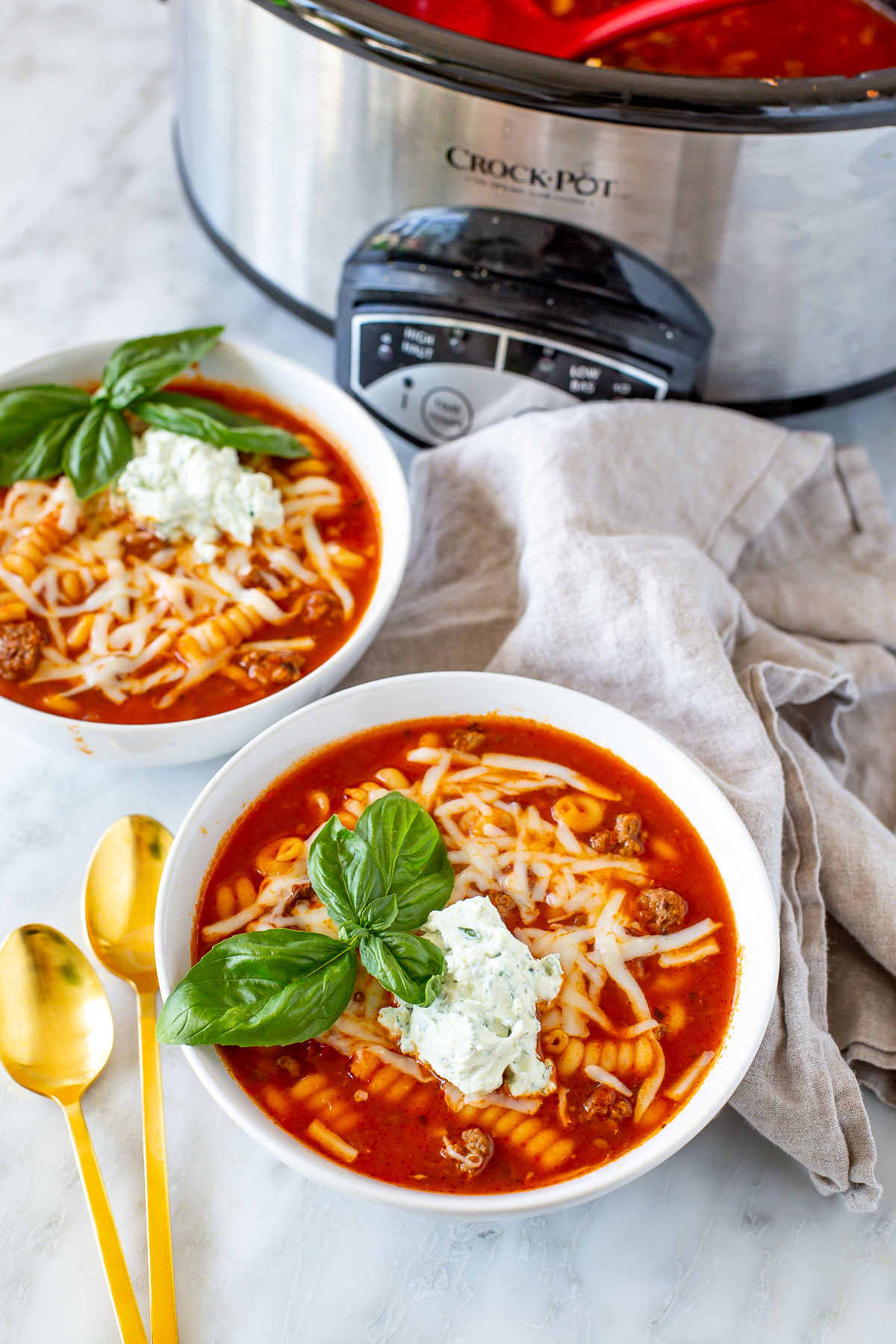 Side shot of two bowls of Easy Crockpot Lasagna Soup with a gold spoon and a crockpot.