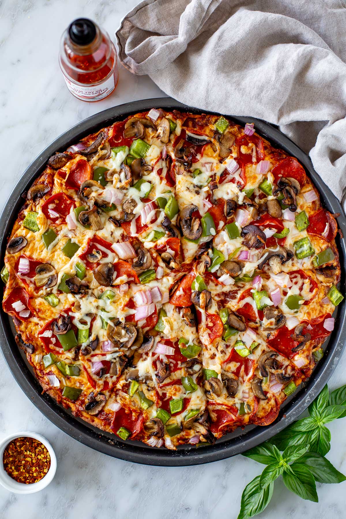 Overhead shot of a whole High Protein Pizza with pepperoni and vegetable toppings in a round pan, sliced into wedges.