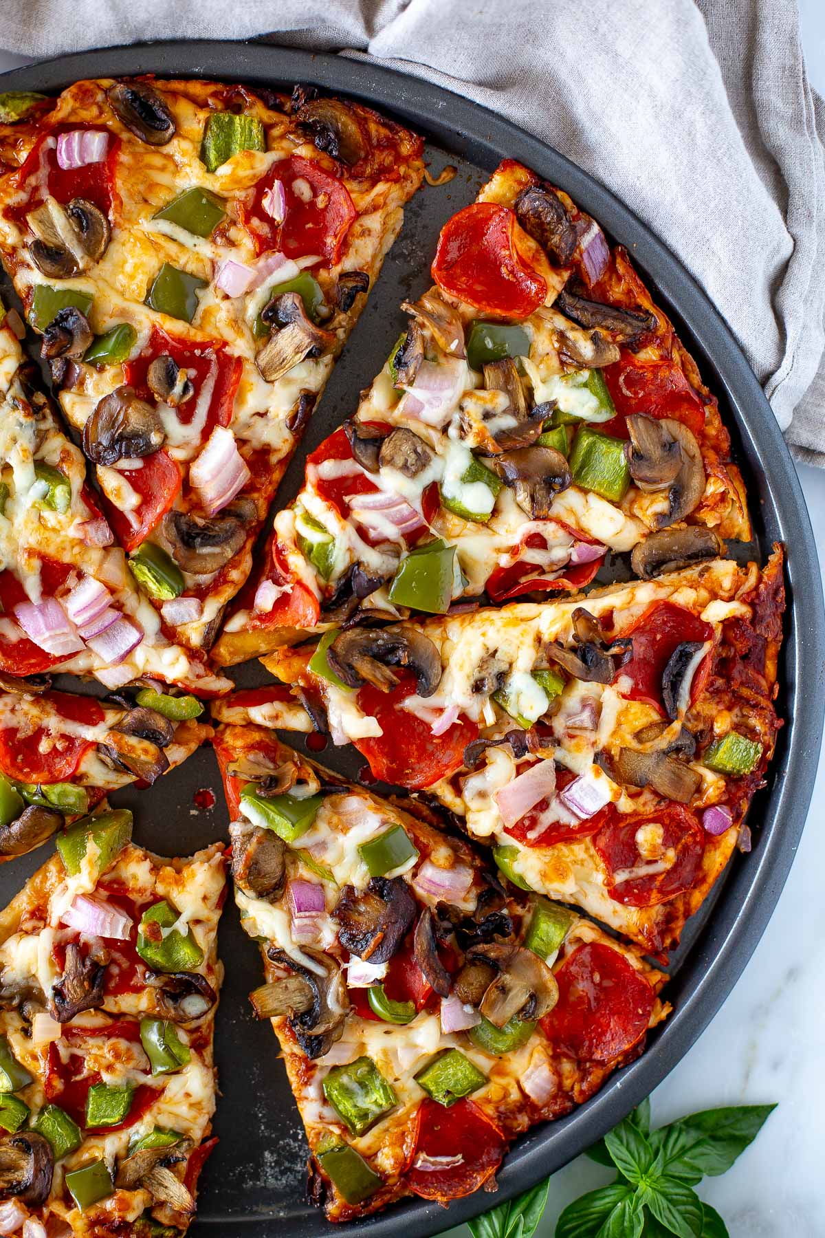 Overhead shot of a sliced High Protein Pizza with pepperoni and vegetable toppings in a round pizza pan.