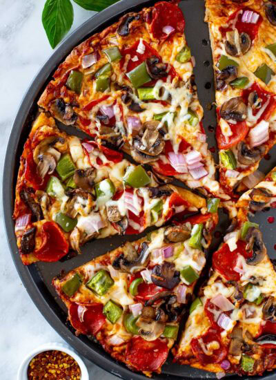 Overhead shot of a sliced High Protein Pizza with pepperoni and vegetable toppings in a round pizza pan.