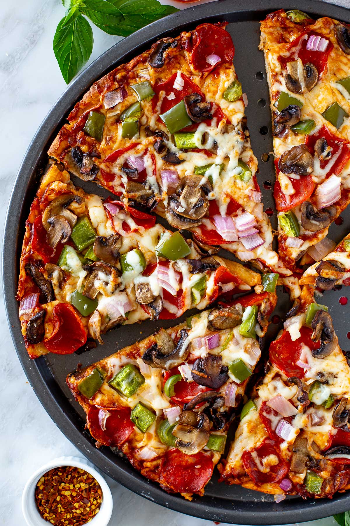 Overhead shot of a sliced High Protein Pizza with pepperoni and vegetable toppings in a round pizza pan.
