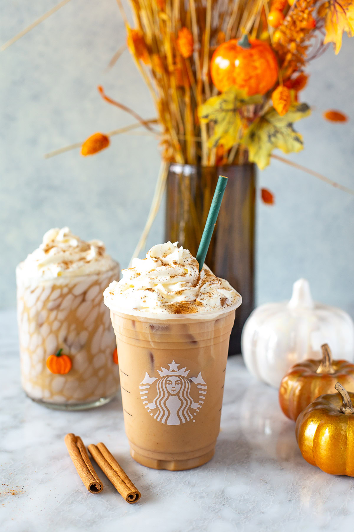 Side shot of an Iced Pumpkin Spice Latte in a Starbucks cup with whipped cream.
