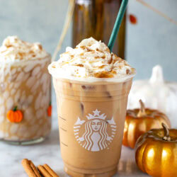 Side shot of an Iced Pumpkin Spice Latte in a Starbucks cup with whipped cream.
