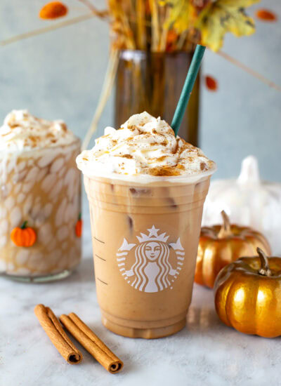 Side shot of an Iced Pumpkin Spice Latte in a Starbucks cup with whipped cream.