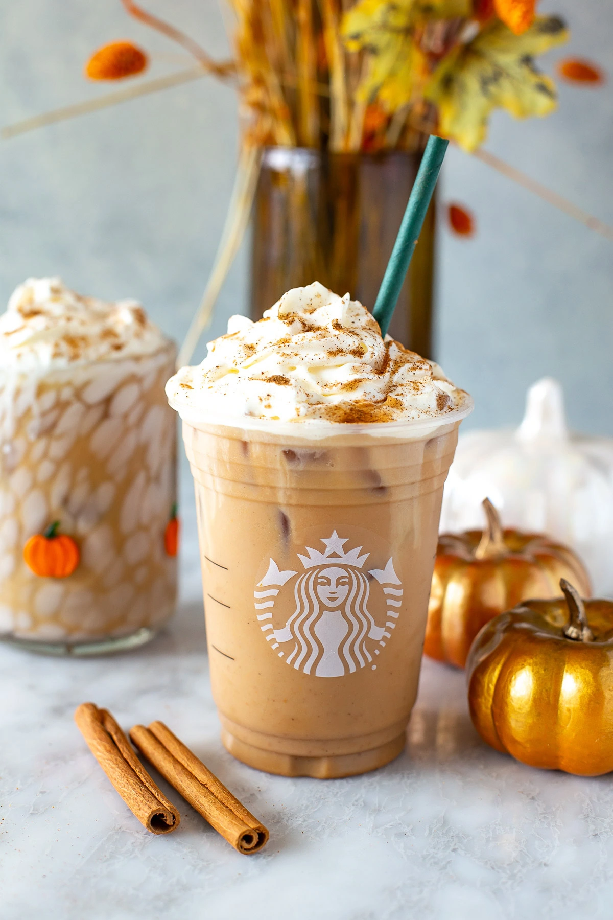Side shot of an Iced Pumpkin Spice Latte in a Starbucks cup with whipped cream.