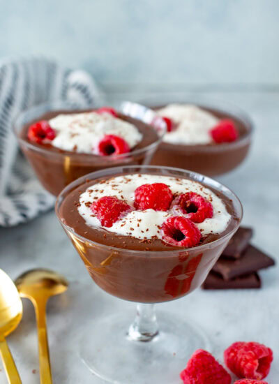 Side shot of three servings of Protein Chocolate Mousse in stemmed glasses, topped with whipped cream and raspberries.