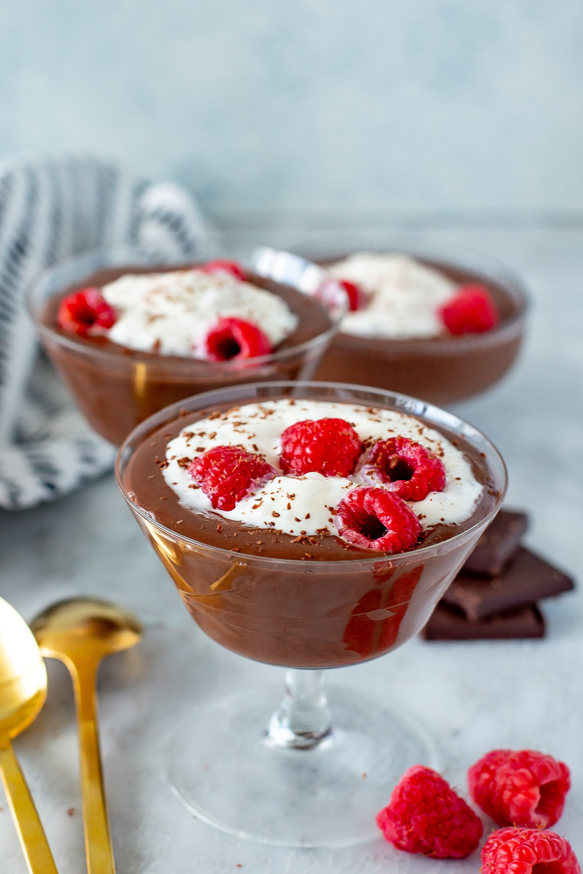 Side shot of three servings of Protein Chocolate Mousse in stemmed glasses, topped with whipped cream and raspberries.