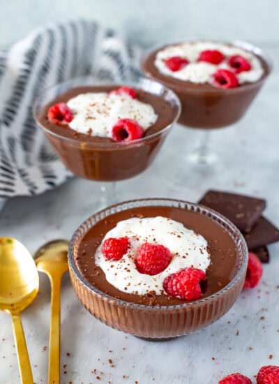 Side shot of three servings of Protein Chocolate Mousse topped with whipped cream and raspberries.
