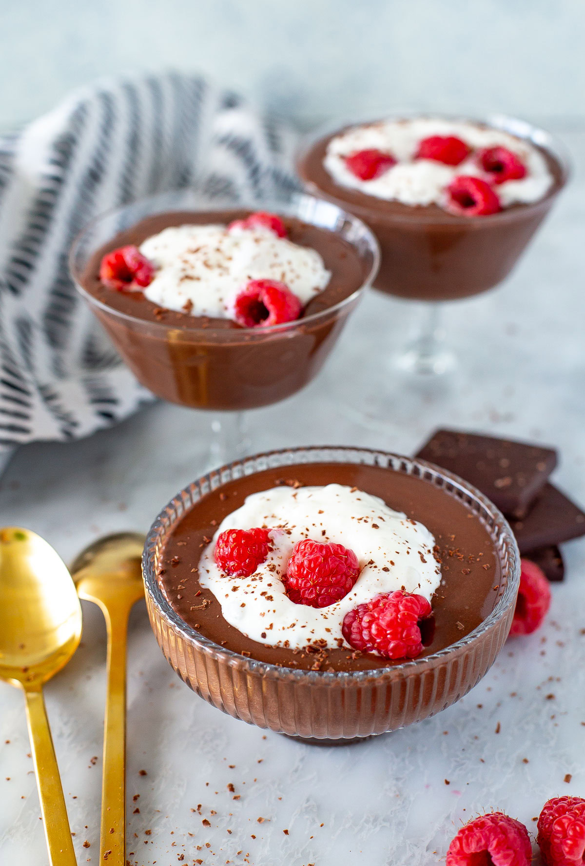 Side shot of three servings of Protein Chocolate Mousse topped with whipped cream and raspberries.