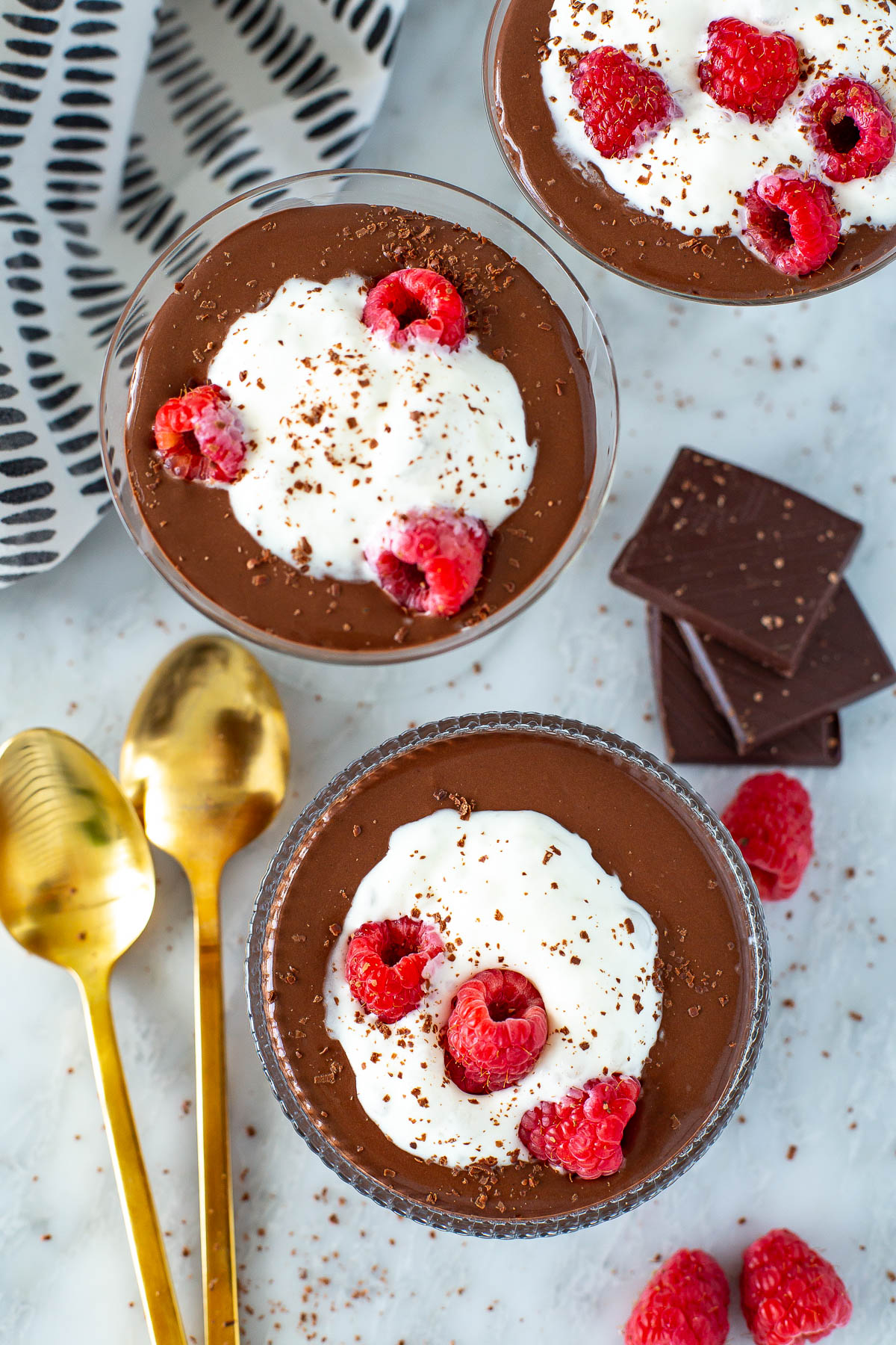 Overhead shot of three servings of Protein Chocolate Mousse topped with whipped cream and raspberries.