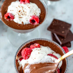 Overhead shot of three servings of Protein Chocolate Mousse topped with whipped cream and raspberries.