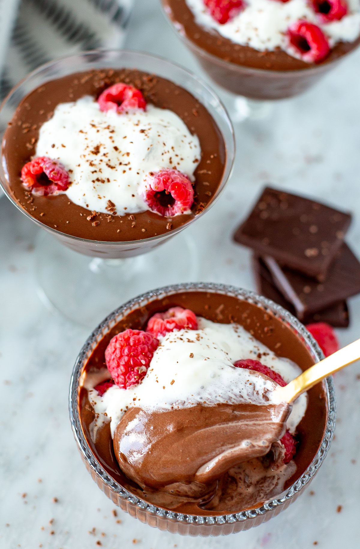 Overhead shot of three servings of Protein Chocolate Mousse topped with whipped cream and raspberries.