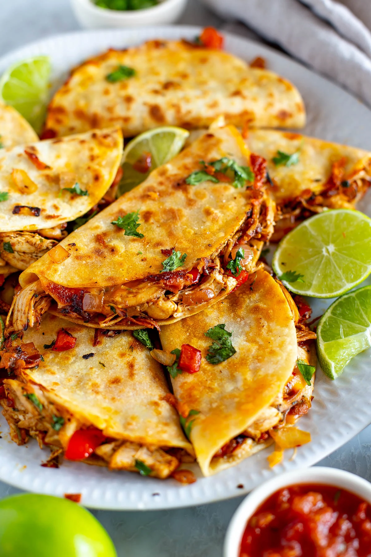 Overhead shot of Cheesy Pulled Chicken Tacos on a white plate with lime wedges and a side of salsa.