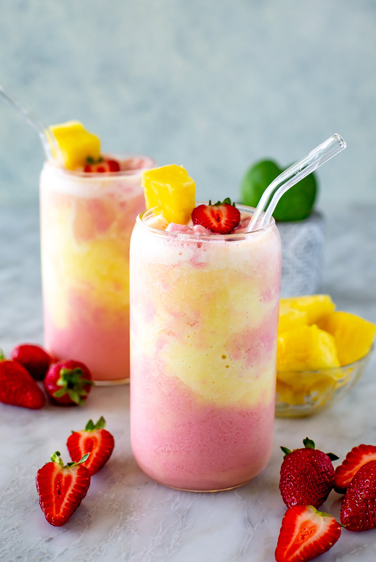 Side shot of two glass of strawberry pineapple smoothie with a straw.