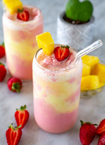 Side shot of a strawberry pineapple smoothie with a straw.