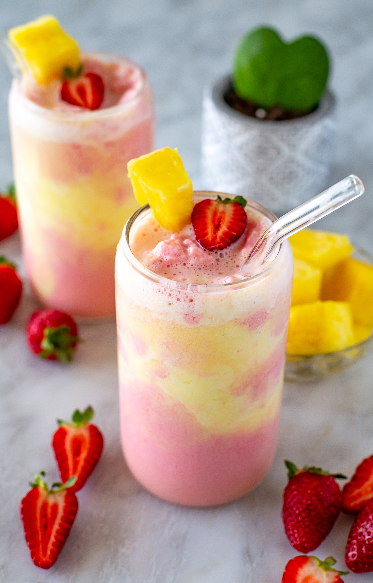 Side shot of a strawberry pineapple smoothie with a straw.